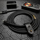 Black charging cable coiled with leather strap, next to wall plug and power bank