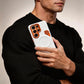 Person holding a white leather-style phone case with orange detail in a black sweater.