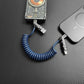 Blue coiled universal cable with metallic connectors charging a mobile device.